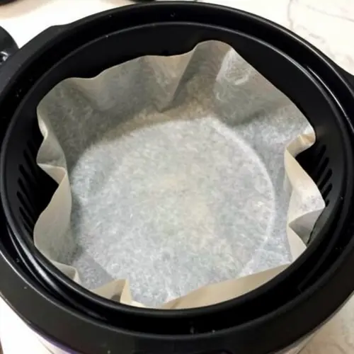 Se puede meter papel vegetal o aluminio en la freidora de aire con una base bien ajustada y alimento colocado encima en una cocina doméstica