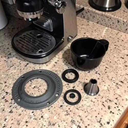 Las piezas de una cafetera que más se desgastan colocadas sobre una encimera con juntas, filtro y boquilla desmontables