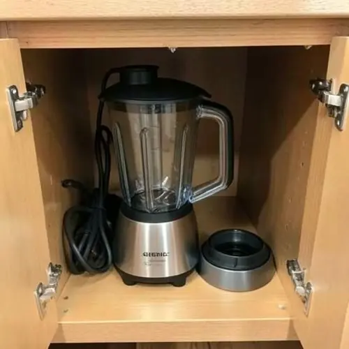 Licuadora guardada con piezas secas, cable recogido y hueco de armario accesible en una cocina real